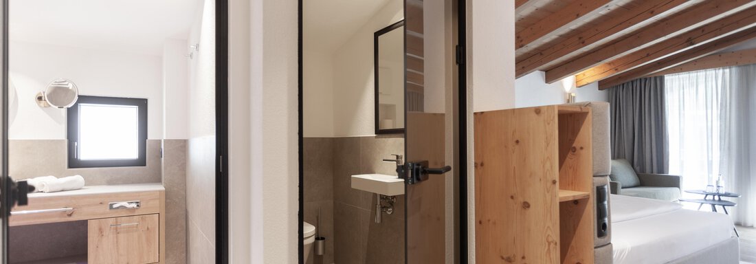 A modern room with a bedroom and a bathroom. The decor is bright and inviting, with wood details and large windows. - Hotel Hubertus - Sölden
