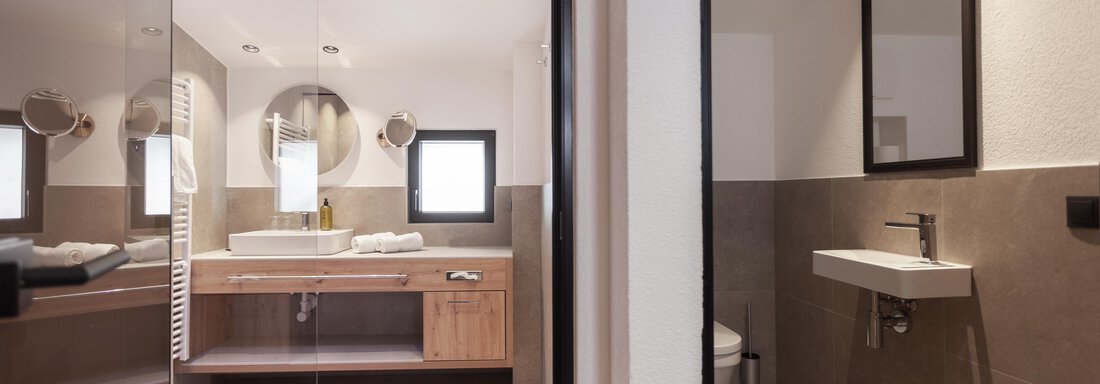 A modern bathroom with elegant fixtures and wooden shelves. The bright design offers an inviting atmosphere. - Hotel Hubertus - Sölden