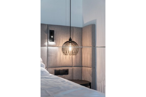 A modern bedroom with a stylish bed and a decorative pendant light. The walls are painted in neutral tones, creating a relaxed atmosphere. - Hotel Hubertus - Sölden