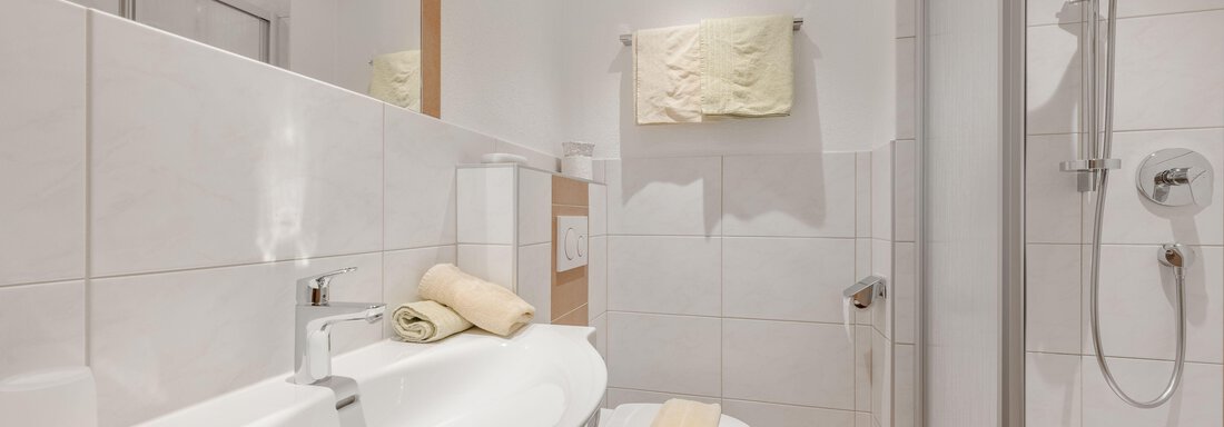 A modern bathroom with white tiles and an elegant sink. A shower niche and towels in soft colors complete the picture. - Pension Charly - Sölden