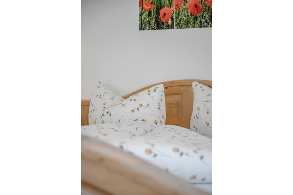 A cozy bed with floral bedding and pillows. In the background, there is a picture of red poppies. - Pension Charly - Sölden