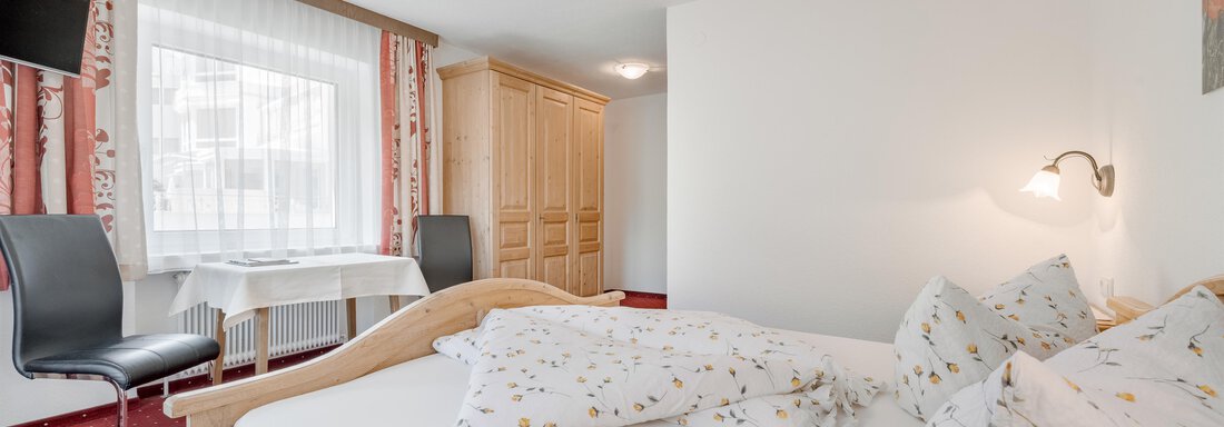A cozy bedroom with a large bed and colorful pillows. The room features a table, a chair, and a television. - Pension Charly - Sölden