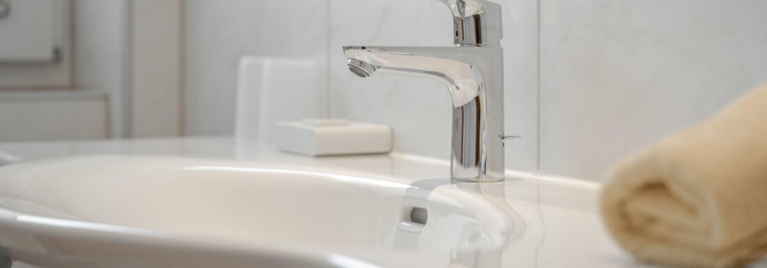 A modern washbasin with an elegant faucet. On it lie a piece of soap and a neatly folded towel. - Pension Charly - Sölden