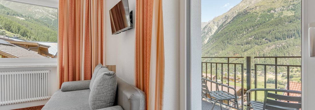 A modern room with a gray sofa and a television wall. The balcony offers a view of the mountains and the clear sky landscape. - Pension Charly - Sölden