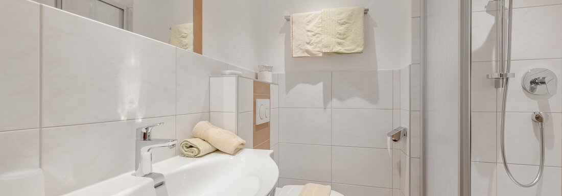 A modern bathroom with white tiles and a large sink. The shower is clearly separated, and some towels are neatly placed. - Pension Charly - Sölden