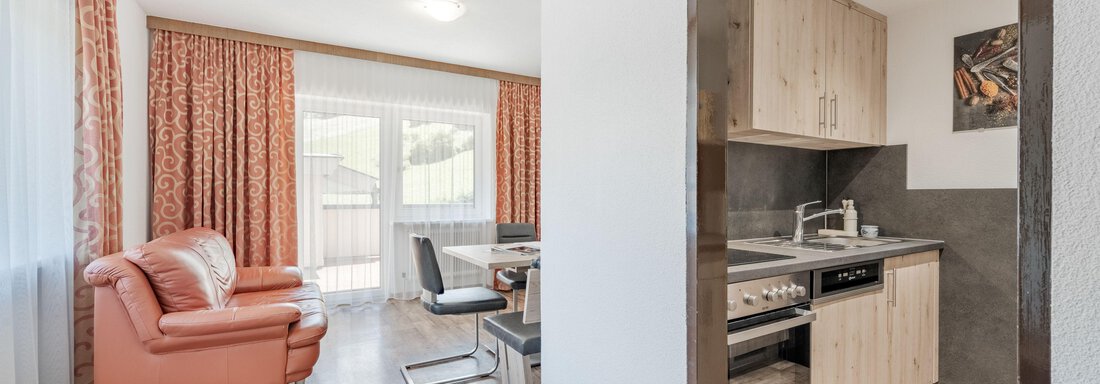 A modern apartment with a cozy living room and an open kitchen. The decor is bright and inviting, with a large window that lets in plenty of light. - Pension Charly - Sölden