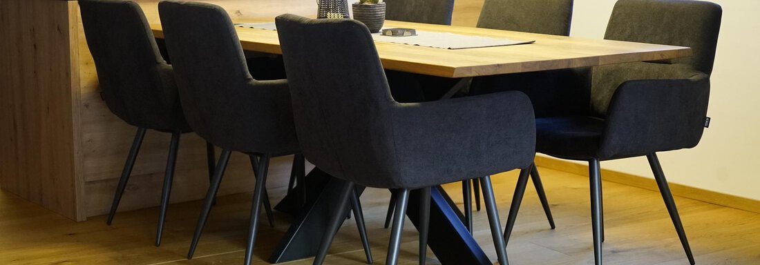 A modern dining area with a large wooden table and six elegant chairs. The room has a bright, inviting atmosphere and is decorated with plants. - Pension "Zur alten Mühle" - Sölden
