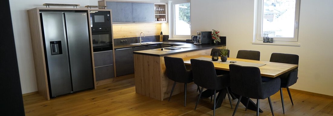 Modern kitchen with wooden floor and large windows. The dining area is equipped with a wooden chair and an elegant lamp. - Pension "Zur alten Mühle" - Sölden