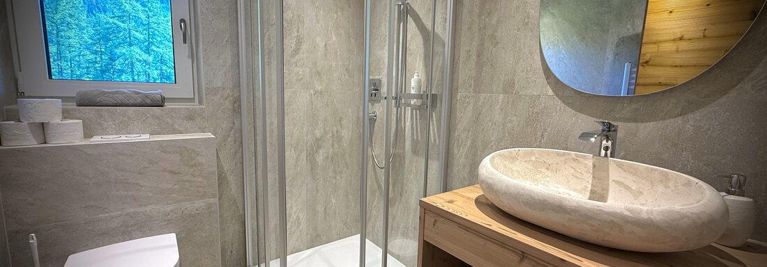 Ein modernes Badezimmer mit einer Glasdusche und einem runden Marmorwaschbecken. Große Fenster lassen natürliches Licht herein und schaffen eine angenehme Atmosphäre. - Pension "Zur alten Mühle" - Sölden