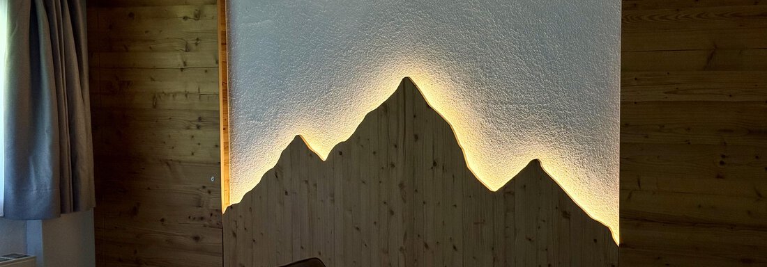 A modern room with wooden paneling and a stylized mountain motif on the wall. Soft lighting emphasizes the contours of the mountains. - Pension "Zur alten Mühle" - Sölden