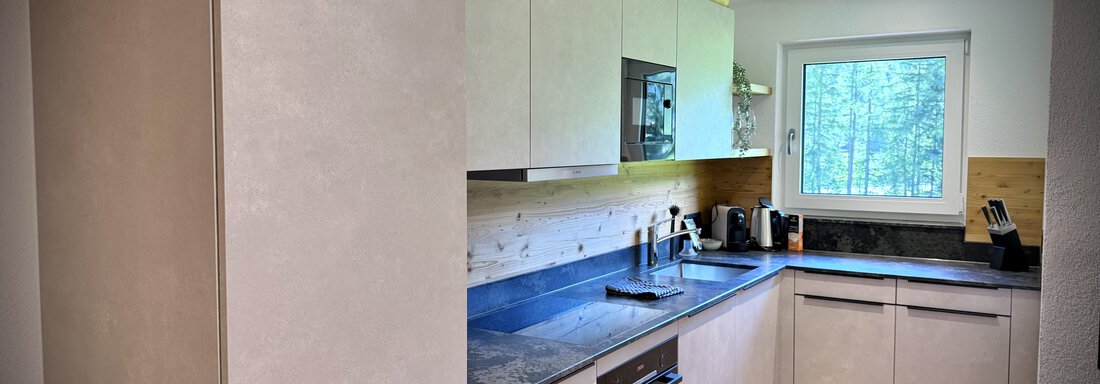 A modern kitchen with light cabinets and a dark countertop. The window offers a view outside to nature. - Pension "Zur alten Mühle" - Sölden
