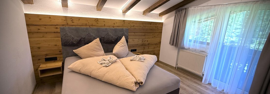 Ein modernes Schlafzimmer mit einem großen Bett und Holzverkleidung. Helle Fenster lassen viel Licht herein und schaffen eine gemütliche Atmosphäre. - Pension "Zur alten Mühle" - Sölden