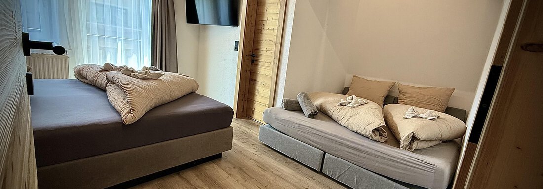 Ein modernes Zimmer mit einem Doppelbett und einem Schlafsofa. Der Raum hat große Fenster mit viel natürlichem Licht und ein Holzdesign. - Pension "Zur alten Mühle" - Sölden