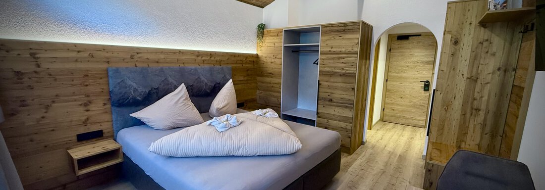 A modern bedroom with wooden walls and a comfortable bed. The room is bright and designed to be cozy. - Pension "Zur alten Mühle" - Sölden