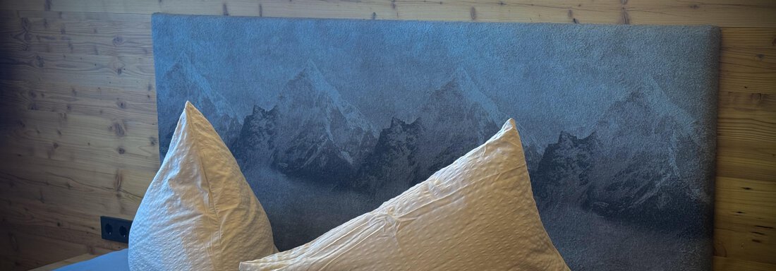 Ein gemütliches Schlafzimmer mit einem modernen Kopfteil und großen Kissen. Die Wand ist aus Holz, was eine warme Atmosphäre schafft. - Pension "Zur alten Mühle" - Sölden