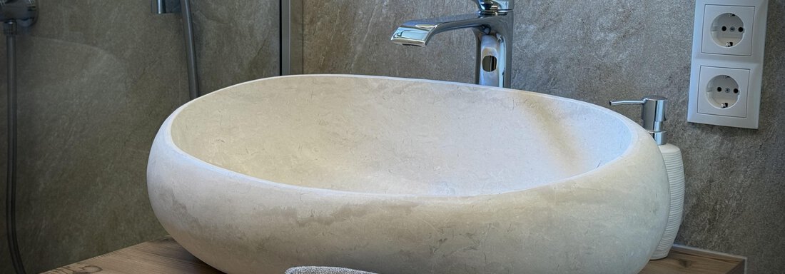 An elegant stone sink stands on a wooden stand. Next to it lies a gray towel on the wooden surface. - Pension "Zur alten Mühle" - Sölden
