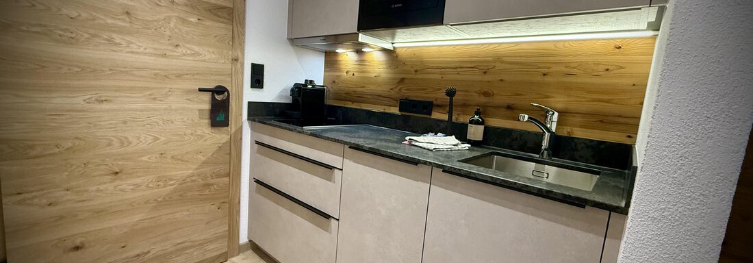 Eine moderne Küche mit hellen Holzelementen und schwarzen Oberflächen. Sie ist gut ausgestattet und bietet eine gemütliche Atmosphäre. - Pension "Zur alten Mühle" - Sölden