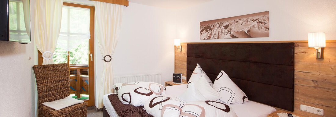 Zimmer A cozy bedroom with a large bed, a TV cabinet, and a window with an outdoor view. The room is designed to be bright and welcoming. - Trofana Appartements - Sölden