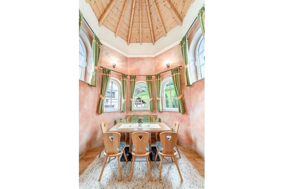 Ein einladender Essbereich mit einem runden Tisch und Holzstühlen. Große Fenster mit grünen Vorhängen bieten einen schönen Blick auf die Umgebung. - Villa Castelbell - Sölden