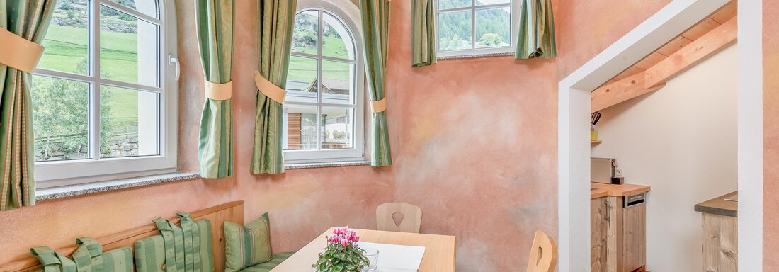 Ein gemütlicher Essbereich mit einer langen Tischfläche und Bänken. Die Wände sind in sanften Farben gestrichen und große Fenster sorgen für viel Licht. - Villa Castelbell - Sölden
