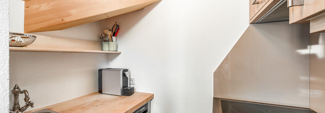 Eine moderne Küche mit Holzregalen und einem schrägen Dach. Die Ausstattung umfasst eine Spüle, einen Herd und eine kleine Küchenzeile. - Villa Castelbell - Sölden