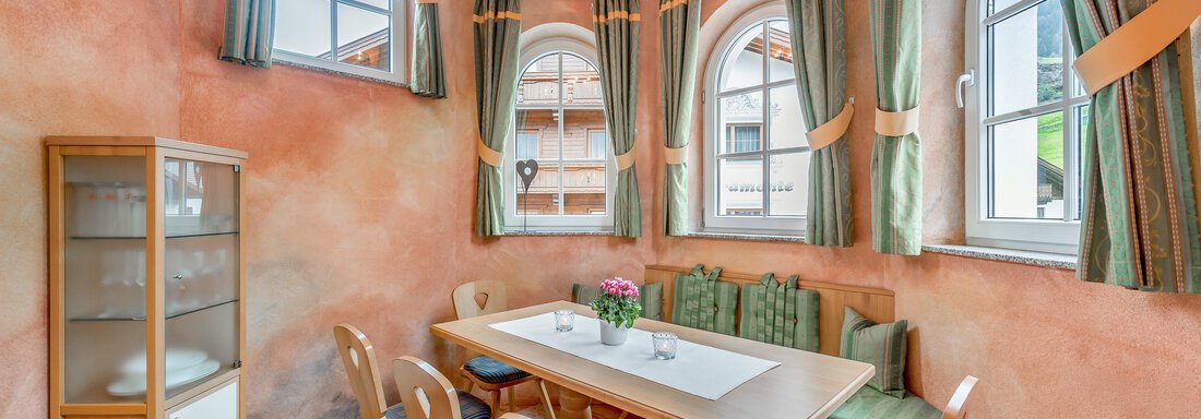 Ein gemütlicher Essbereich mit einer hellen Tischdeko. Die Wände sind in warmen Farbtönen gehalten und große Fenster sorgen für viel Licht. - Villa Castelbell - Sölden