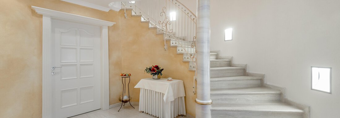 Ein eleganter Eingangsbereich mit einer geschwungenen Treppe. Die Wände sind in warmen Farben gehalten, und es gibt eine kleine Tischdekoration. - Villa Castelbell - Sölden