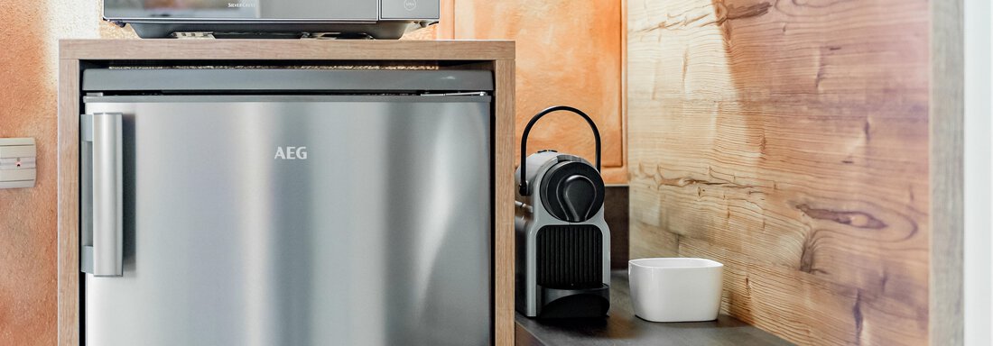 Eine moderne Küche mit einem Kühlschrank und einer Mikrowelle. Neben dem Kühlschrank steht eine Kaffeekapselmaschine und eine weiße Schüssel auf der Arbeitsfläche. - Villa Castelbell - Sölden