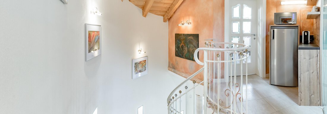 Eine helle Treppe mit einem eleganten Geländer führt in einen modernen Raum. Die Wände sind in warmen Tönen gehalten und es gibt einige Bilder zur Dekoration. - Villa Castelbell - Sölden