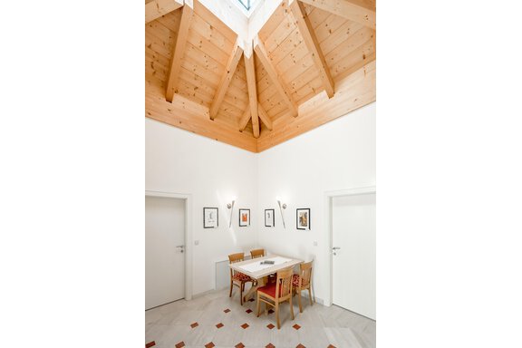 Ein heller Raum mit Holztäfelung und schrägen Wänden. Ein Tisch mit Stühlen steht in der Mitte, umgeben von weißen Türen. - Villa Castelbell - Sölden