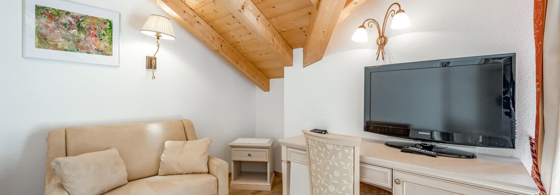 Ein gemütlicher Raum mit Holzdecke, einem Sofa und einem Schreibtisch. Ein Fernseher und eine kleine Kommode ergänzen die Einrichtung. - Villa Castelbell - Sölden