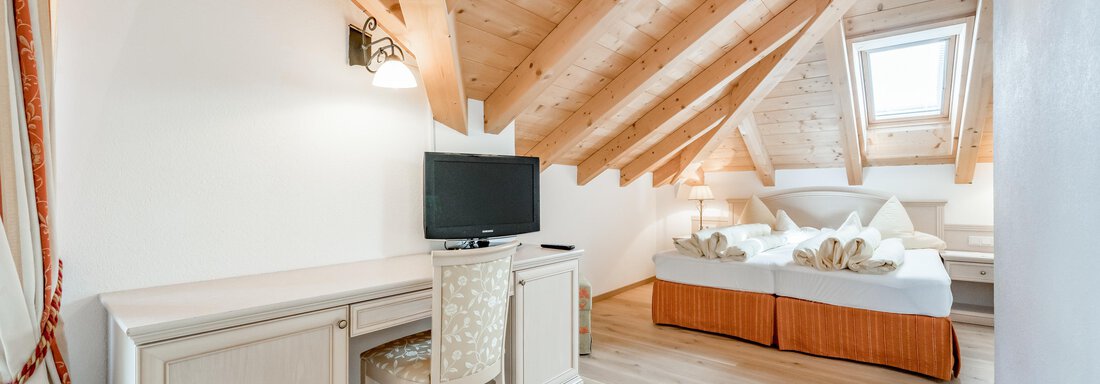 Ein gemütliches Schlafzimmer mit einer schrägen Holzdecke und einem großen Bett. Es gibt einen Schreibtisch mit Stuhl und einen Fernseher. - Villa Castelbell - Sölden