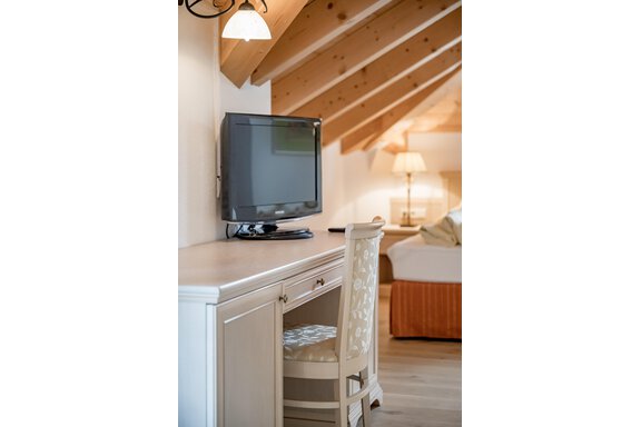 Ein gemütlicher Raum mit einem Schreibtisch und einem Fernseher. Die Holzbalkendecke und das orangefarbene Bett sorgen für eine warme Atmosphäre. - Villa Castelbell - Sölden