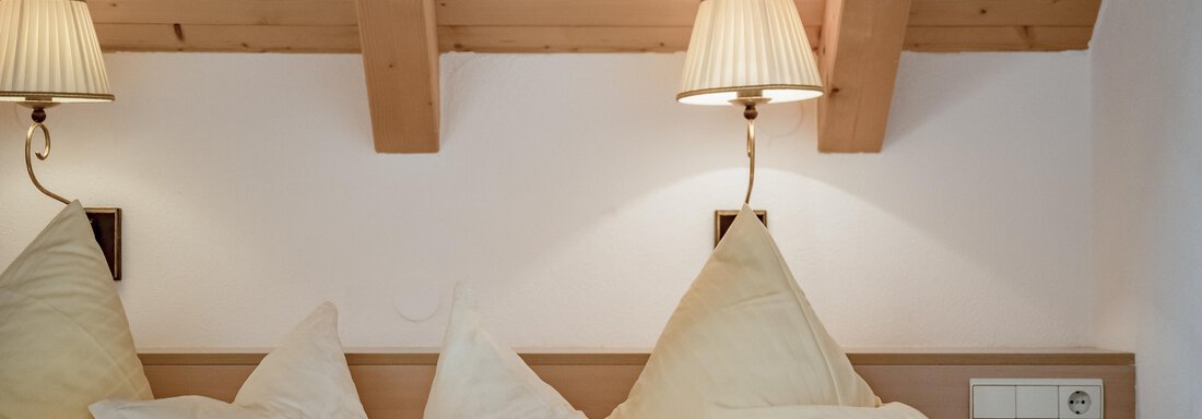 Ein gemütliches Schlafzimmer mit Holzdecke und sanfter Beleuchtung. Die Betten sind mit großen, weißen Kissen ausgestattet. - Villa Castelbell - Sölden