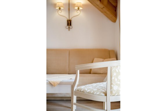 Ein gemütlicher Wohnraum mit einem beigen Sofa und einem weißen Stuhl. Die Wände sind hell, und zwei Wandleuchten sorgen für sanftes Licht. - Villa Castelbell - Sölden