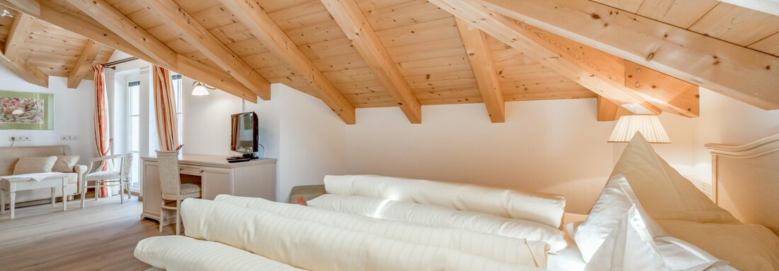 Ein gemütliches Schlafzimmer mit Holzdecke und mehreren Kissen. Der Raum ist hell und einladend mit einem Fernseher in der Ecke. - Villa Castelbell - Sölden