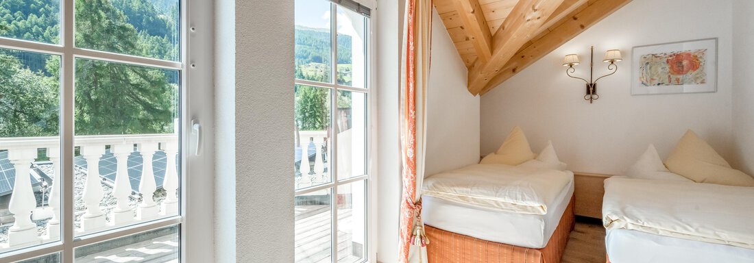 Ein helles Zimmer mit zwei Betten und Holzdecke. Große Fenster bieten einen Blick auf die Berge und Zugang zu einem Balkon. - Villa Castelbell - Sölden