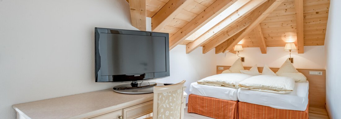 Ein gemütliches Zimmer mit Dachschrägen und Holzbalken. Es gibt ein Doppelbett, einen Tisch mit Stuhl und einen Fernseher. - Villa Castelbell - Sölden