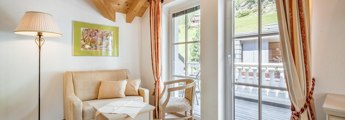A bright and modern living room with a wooden ceiling and large windows. There is a sofa, a coffee table, and a chair. - Villa Castelbell - Sölden