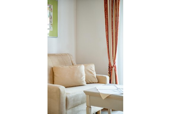 A cozy living room with a beige sofa and a small table. The windows are decorated with elegant curtains. - Villa Castelbell - Sölden
