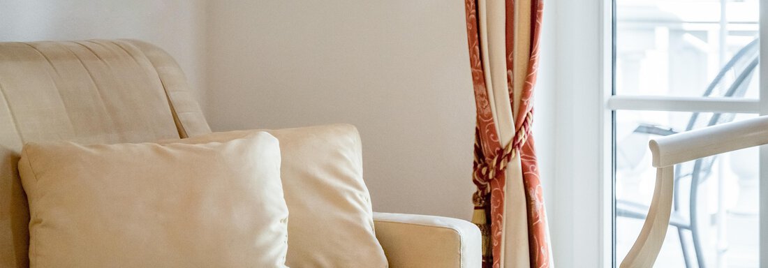 A cozy living room with a beige sofa and a table.  
Curtains in warm colors hang in front of the window. - Villa Castelbell - Sölden