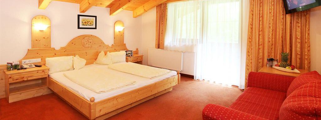 Ein gemütliches Schlafzimmer mit Holzdekor, einem großen Bett und einem roten Sofa. Der Raum hat große Fenster, die viel Licht hereinlassen. - Waldele - Sölden