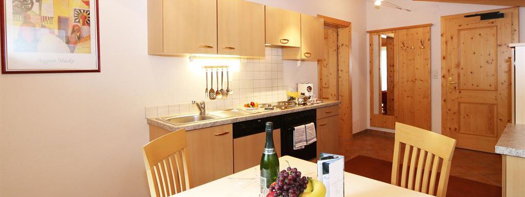 Eine helle Küche mit Holzregalen und moderner Ausstattung. Am Tisch stehen frisches Obst und eine Flasche Sekt. - Waldele - Sölden