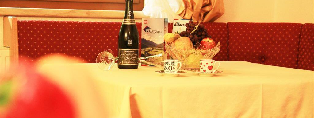 Ein schön gedeckter Tisch mit einer Flasche Sekt und frischem Obst. Die gemütliche Atmosphäre wird durch die roten Polster und das Tageslicht unterstrichen. - Waldele - Sölden