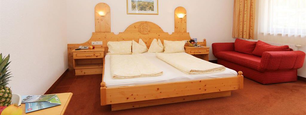 Ein gemütliches Hotelzimmer mit einem Doppelbett und einem roten Sofa. Der Raum hat helle Wände und ist gut beleuchtet. - Waldele - Sölden