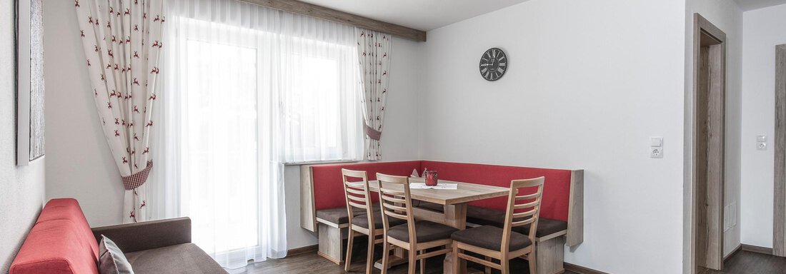 Ein modernes Wohnzimmer mit einer roten Couch und einem Esstisch für mehrere Personen. Große Fenster sorgen für viel Tageslicht. - Zenz´n Hof - Sölden