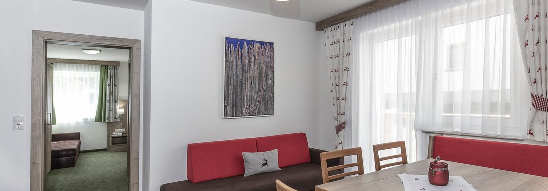 Ein modernes Wohnzimmer mit einem Esstisch und gemütlicher Sitzecke. Große Fenster sorgen für viel Tageslicht und eine angenehme Atmosphäre. - Zenz´n Hof - Sölden