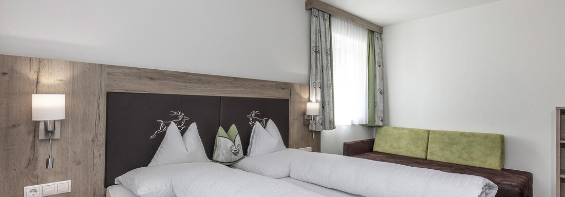 Ein gemütliches Schlafzimmer mit zwei Einzelbetten und modernem Design. Die Wände sind hell, und es gibt eine grüne Sitzecke sowie Fenster mit Vorhängen. - Zenz´n Hof - Sölden
