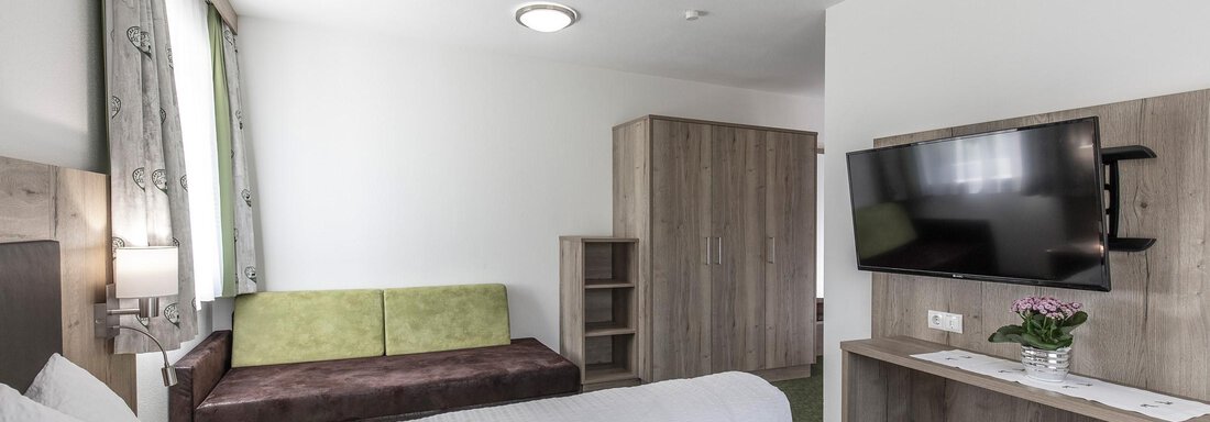 Ein modernes Hotelzimmer mit einem Doppelbett, einem Sofa und einem Fernseher. Die Wände sind hell und es gibt einen Kleiderschrank aus Holz. - Zenz´n Hof - Sölden