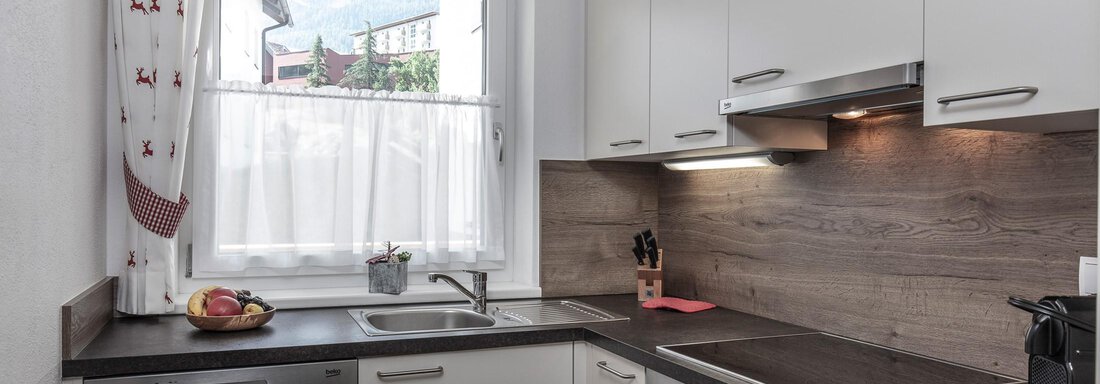 Eine moderne Küche mit hellen Schränken und Holzdetails. Ein Fenster lässt Tageslicht herein und es sind Obst und Küchengeräte auf der Arbeitsplatte sichtbar. - Zenz´n Hof - Sölden